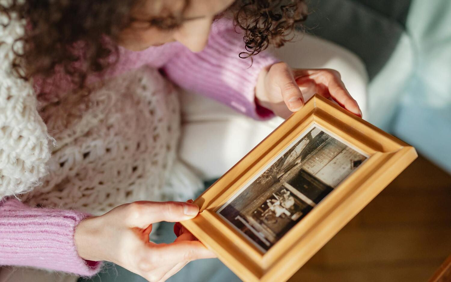 A young woman holding a gold-framed photo at home
