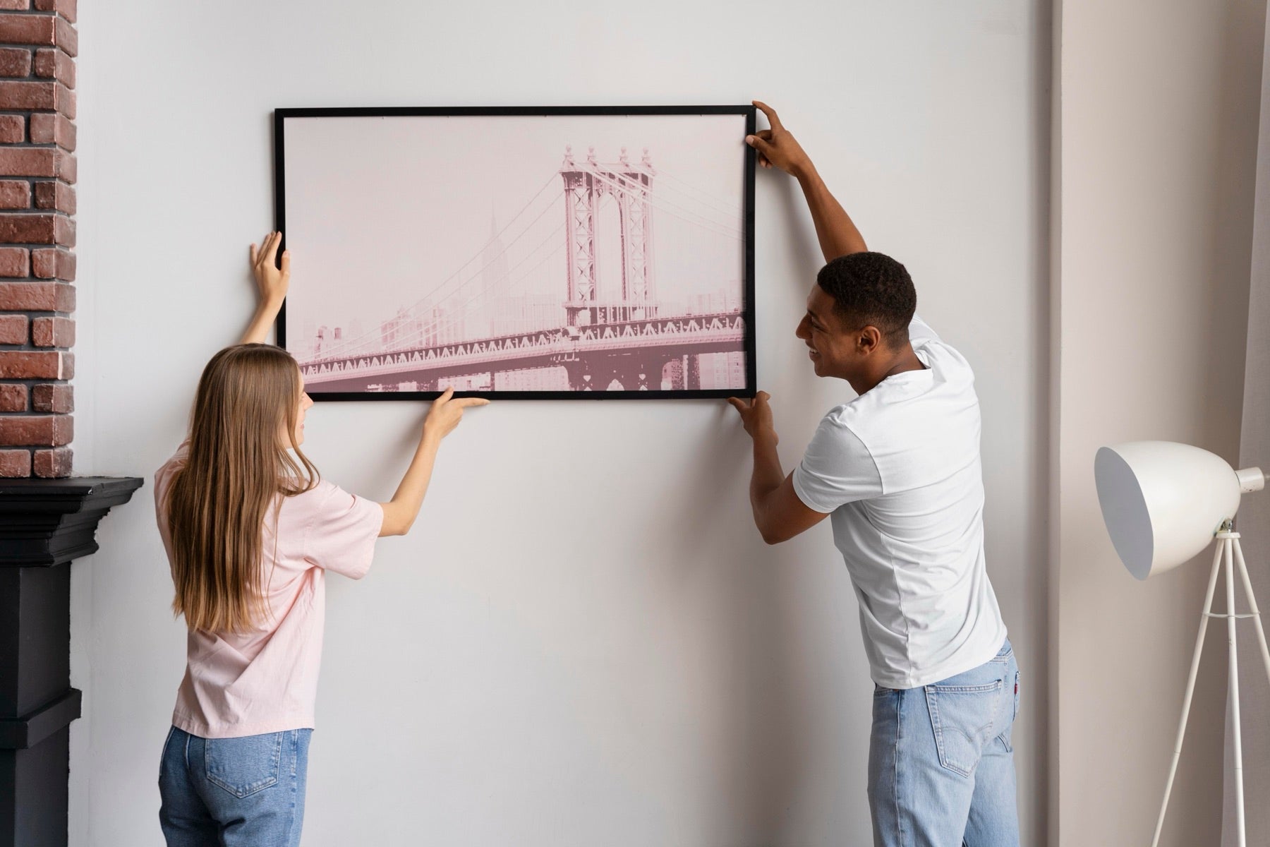Two people hanging a framed print together on a wall