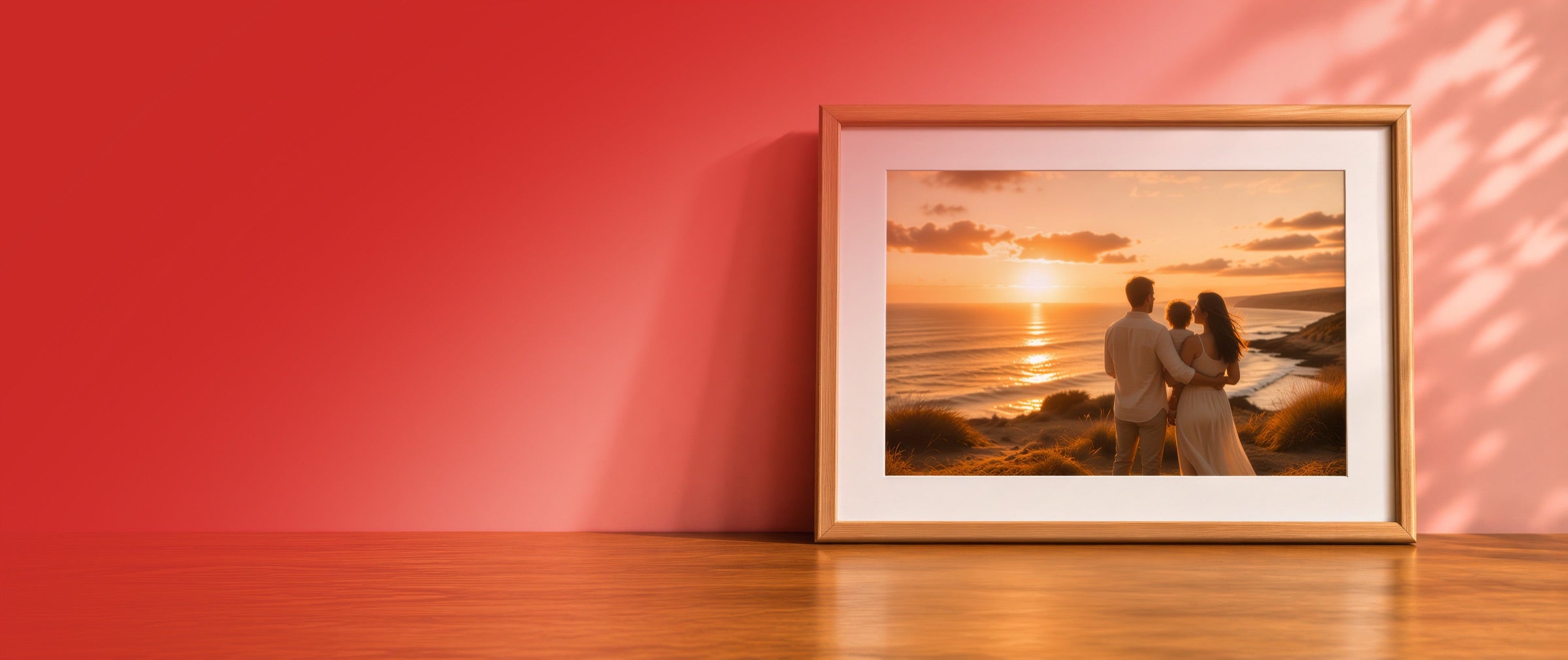 A framed sunset photograph leaning against a red wall on a wooden tabletop
